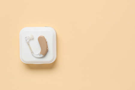 Box with hearing aid on color background