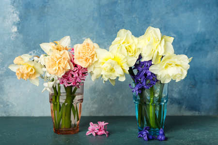 Vases with beautiful flowers on color background