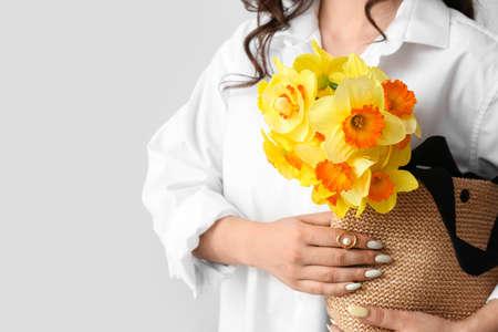 Young woman with beautiful bouquet of narcissus flowers in bag on light backgroundの写真素材