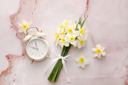Composition with beautiful narcissus flowers and alarm clock on color background