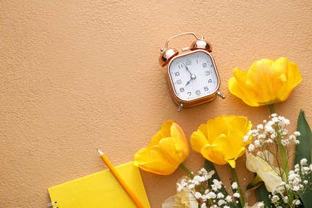 Composition with beautiful flowers and alarm clock on color background