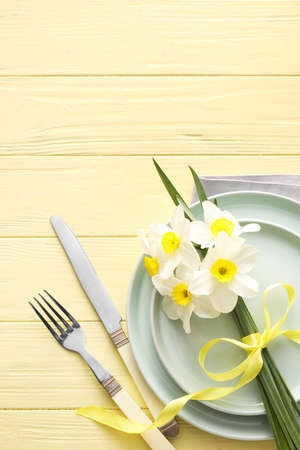 Beautiful table setting with narcissus flowers on color wooden backgroundの写真素材