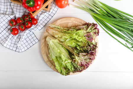 Board with fresh Lollo Rosso lettuce on white wooden background