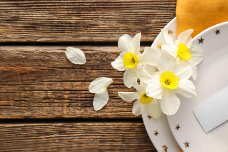 Beautiful table setting with narcissus flowers on wooden background, closeup