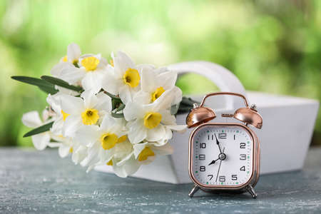 Basket with beautiful narcissus flowers and alarm clock on table outdoors