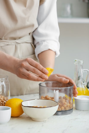 Woman squeezing lemon into blender with chickpeas on table in kitchen, closeupの写真素材