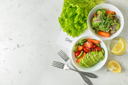 Bowls with delicious vegetable salad and paper sheet with word DIET on light backgroundの写真素材