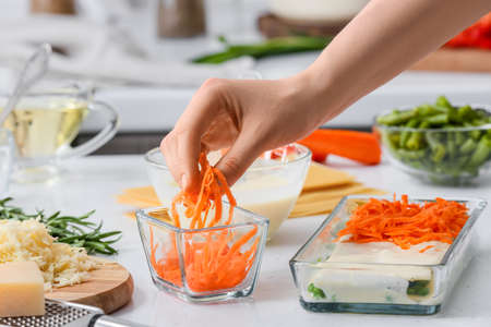 Woman preparing tasty vegetable lasagna on table in kitchenの写真素材