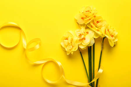 Bouquet of beautiful narcissus flowers and ribbon on color backgroundの写真素材