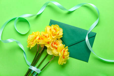 Bouquet of beautiful narcissus flowers and envelope on color background