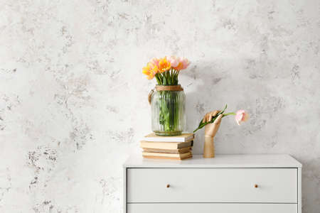 Wooden hand with beautiful tulip flowers on chest of drawers near light wall