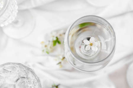 Glass of water and blooming branches on light background