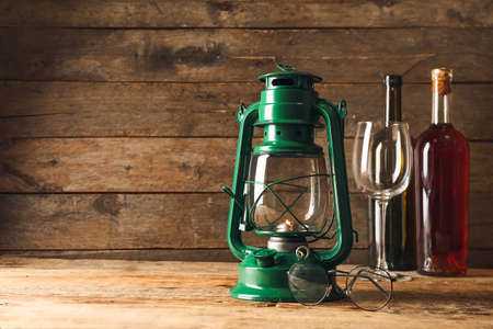 Stylish retro lamp, eyeglasses and bottles of wine on wooden backgroundの写真素材
