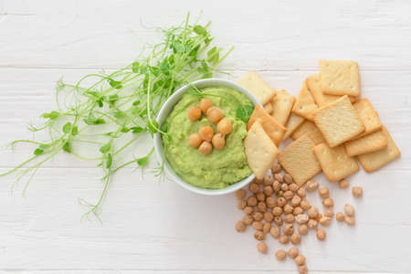 Bowl with tasty green pea hummus, chickpeas and crackers on light wooden backgroundの写真素材