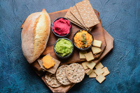 Bowls with tasty hummus, bread and crackers on color background