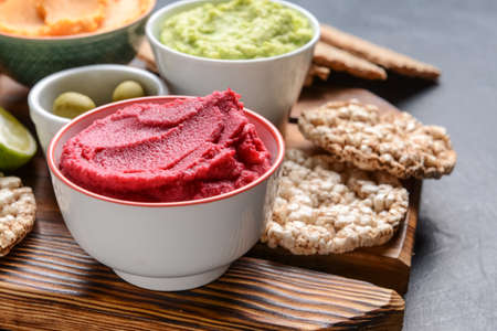 Bowls with tasty beet hummus and rice crackers on dark background, closeupの写真素材
