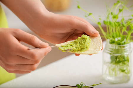 Woman spreading tasty green pea hummus onto pita on light background, closeupの写真素材