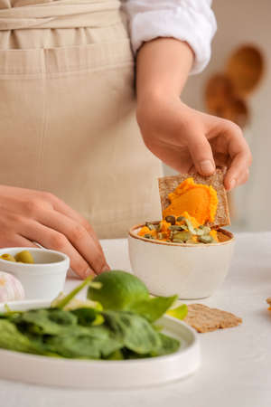 Woman with tasty carrot hummus and cracker on light table, closeupの写真素材
