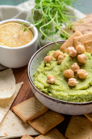 Bowl with tasty green pea hummus, chickpeas and crackers on table, closeupの写真素材