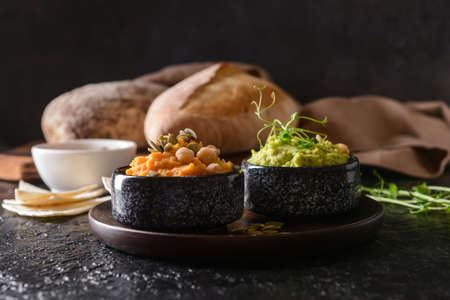 Bowls with tasty hummus, pumpkin seeds and chickpeas on dark background
