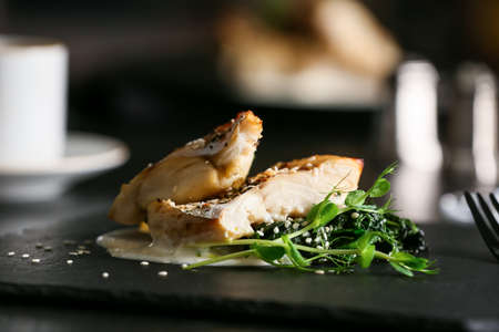 Board with baked cod fillet, pesto sauce and greens on table in restaurant, closeupの写真素材