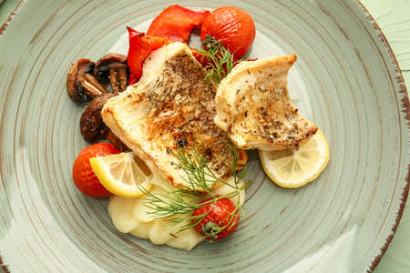 Plate with tasty baked cod fillet, vegetables and mashed potatoes on color wooden background,...
