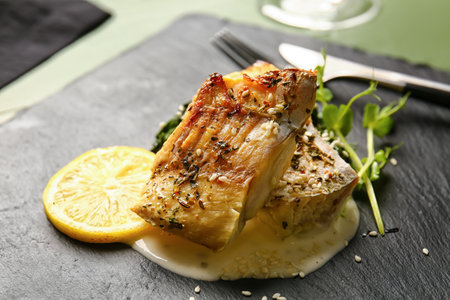 Board with delicious baked cod fillet, sauce and lemon on table in restaurant, closeupの写真素材
