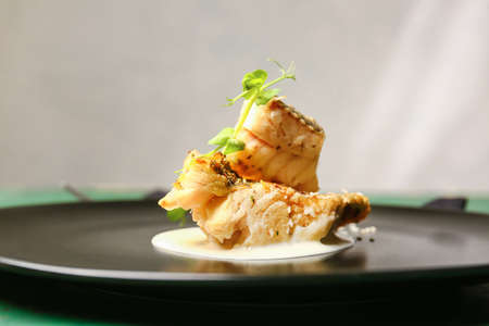 Plate with tasty baked cod fillet, greens and sauce on table, closeup