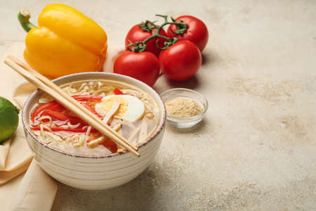 Bowl of tasty Thai soup with vegetables on light background