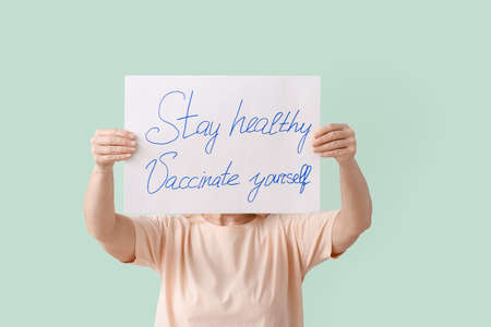 Senior woman holding poster with text STAY HEALTHY - VACCINATE YOURSELF on color backgroundの写真素材