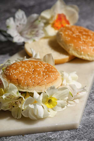 Creative composition with burger buns and narcissus flowers on dark background, closeup