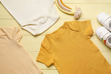 Baby clothes and shoes on color wooden background