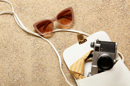 Stylish sunglasses with bag and photo camera on sandの写真素材