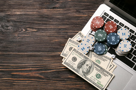 Dices, poker chips, dollar banknotes and laptop on wooden backgroundの写真素材