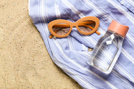 Stylish sunglasses with clothes and bottle of water on sandの写真素材