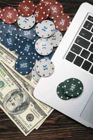 Poker chips, laptop and dollar banknotes on dark wooden background
