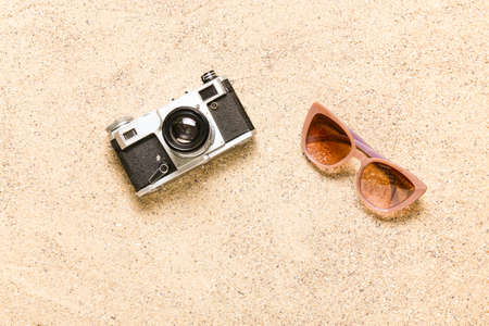 Stylish sunglasses with photo camera on sand