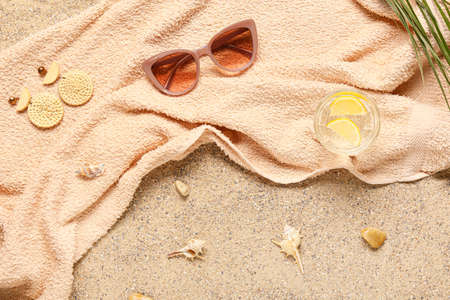 Stylish sunglasses with earrings, towel and glass of water on sandの写真素材