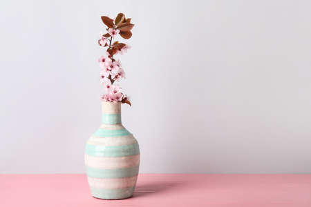 Vase with beautiful blossoming branch on table against light backgroundの写真素材