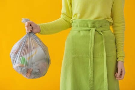 Woman holding bag with garbage on color background, closeup