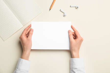 Female hands with blank sheet of paper, notebook, earphones and pencil on color background