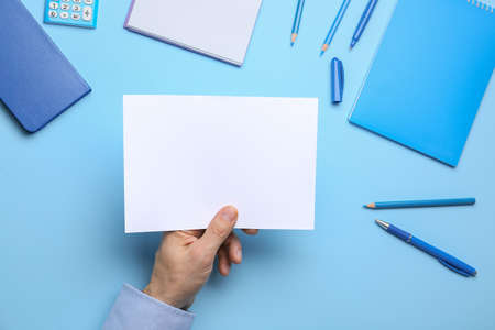 Male hand with blank sheet of paper and stationery on color background