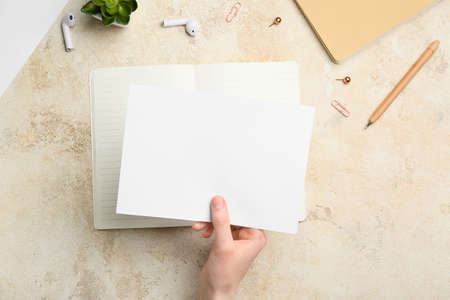 Female hand with blank sheet of paper, earphones and stationery on grunge background