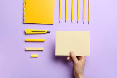 Female hand with blank sheet of paper and stationery on color background