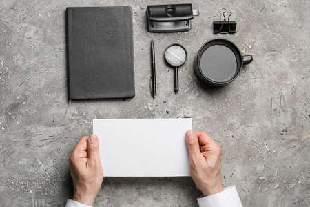 Male hands with blank sheet of paper, cup of coffee and stationery on grunge backgroundの写真素材