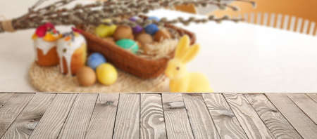 Empty wooden surface and blurred Easter eggs with cakes and pussy willow branches on table