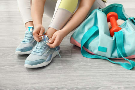 Woman tying shoelaces and bag with dumbbells on light wooden floorの写真素材