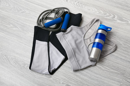 Sportswear, skipping rope and bottle for water on light wooden background