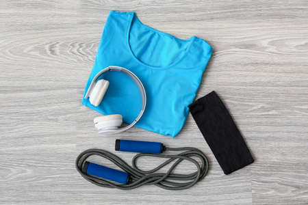 T-shirt, elastic band, skipping rope and headphones on light wooden background