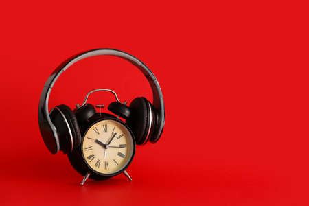 Black vintage alarm clock with headphones on red backgroundの写真素材